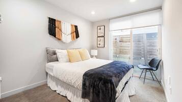 Un dormitorio con cama, una silla, un ventanal y cortina instalada en la pared.