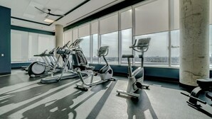 Ein Fitnessstudio mit Trainingsgeräten und großen Fenstern, die einen Blick auf die Stadt ermöglichen.