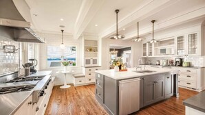 A modern kitchen with white cabinetry, a central island, stainless steel appliances, and a wooden floor.