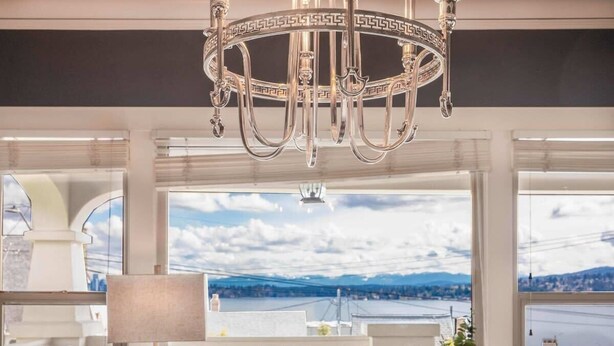 A dining area with a chandelier, a table set for four with floral centerpieces, and a view of a lake and mountains through large windows.