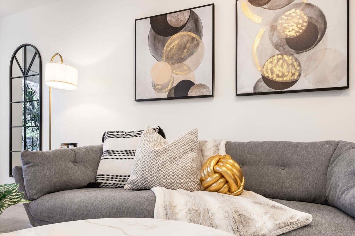 Ein modernes Wohnzimmer mit grauem Sofa, gemusterten Kissen und abstrakter Wandkunst.