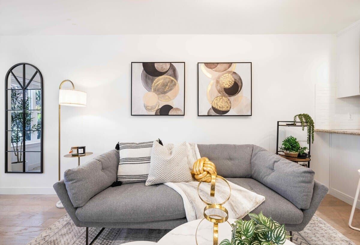 A modern living room with a grey sofa, abstract wall art, a floor lamp, and a small plant.