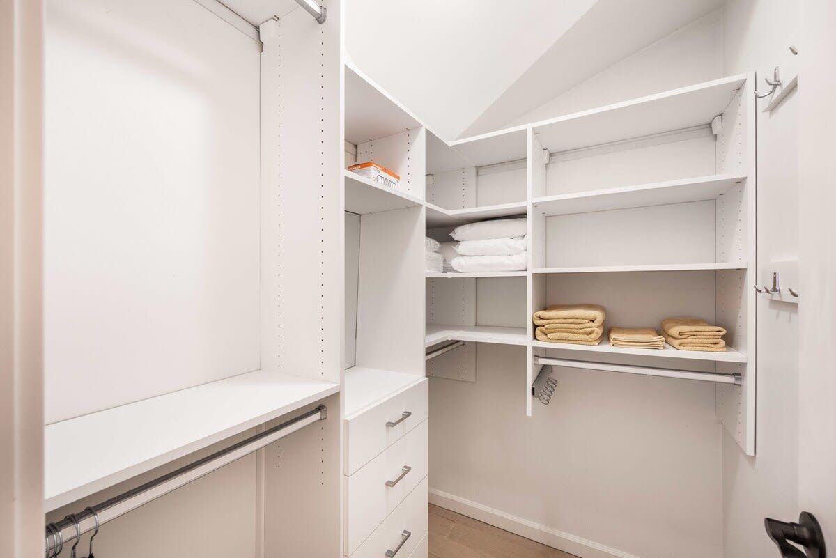 A white closet with open shelves, a hanging rod, and a folded towel rack.