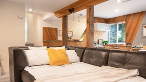 Ein modernes Wohnzimmer mit einer Ledersofa, einem Essbereich mit Tisch und Stühlen sowie einem großen Fenster mit Blick auf Grünflächen.