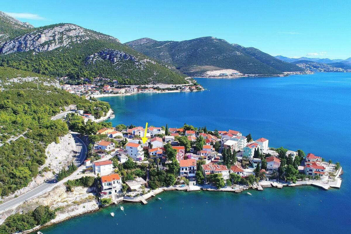A coastal town with buildings along the waterfront, a road leading into the town, and mountains in the background.
