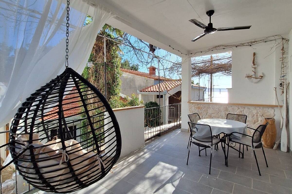 A sunlit patio with a hanging chair, a round table with chairs, and a ceiling fan.