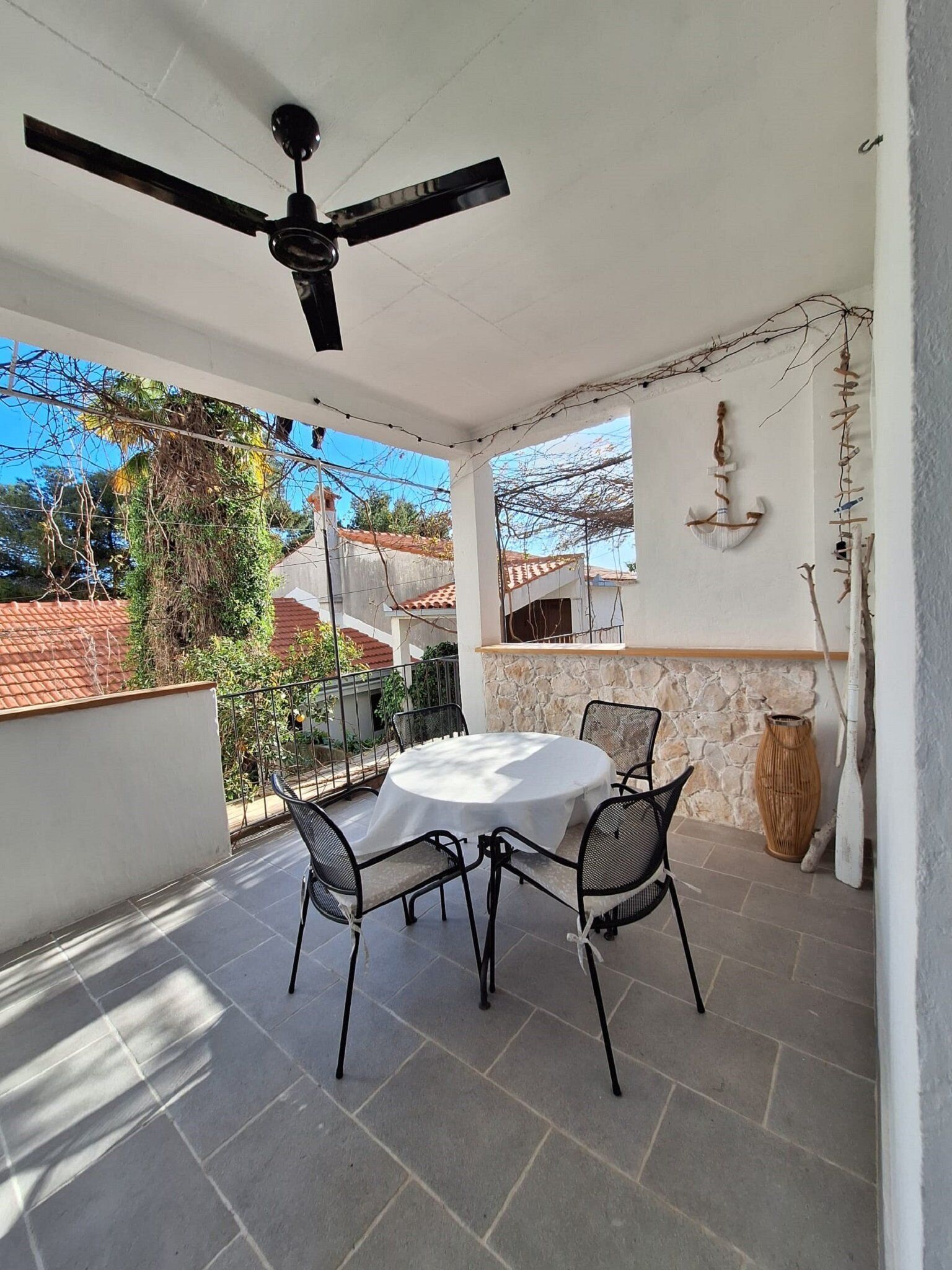 Un patio cubierto con una mesa redonda y sillas, un ventilador de techo, pared de piedra y elementos decorativos.
