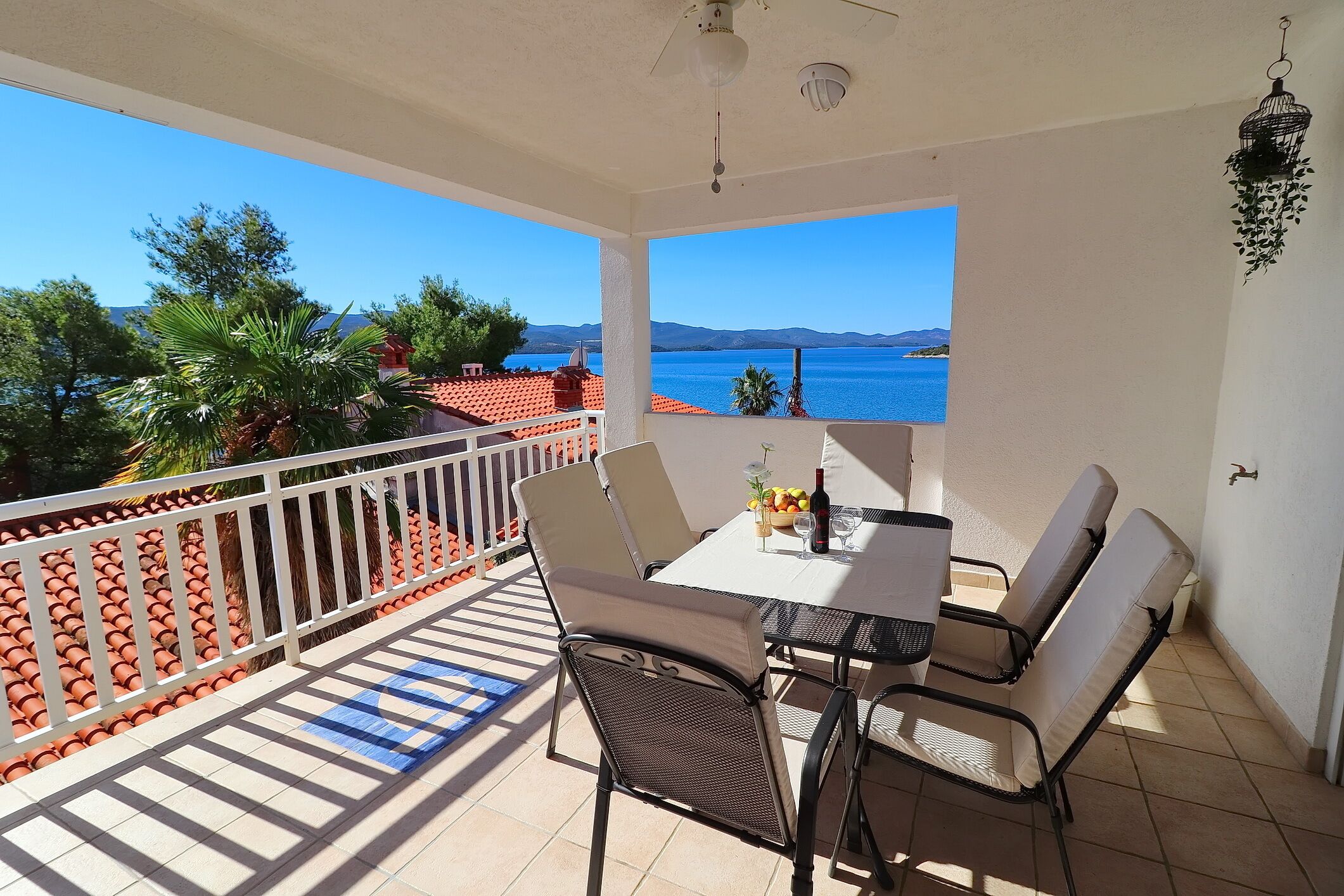 Un balcon avec une table et des chaises, une vue sur la mer et une balustrade blanche.