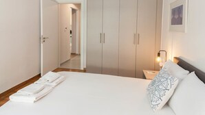 Ein Hotelzimmer mit Bett, Nachttisch, Kleiderschrank und einem zur benachbarten Tür führenden Gang.