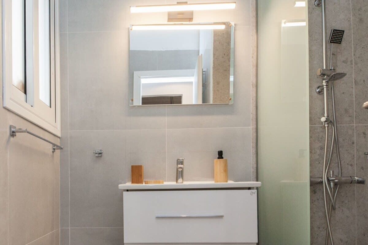 A modern bathroom with a white vanity, a mirror, and a shower area.