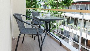 Ein Balkon mit zwei Korbstühlen und einem kleinen Tisch, einer weißen Teekanne und einer Tasse auf dem Tisch.