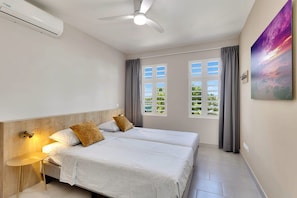 A bedroom with two beds, a ceiling fan, an air conditioning unit, a wall-mounted lamp, and a window with curtains.