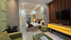A modern hotel room with a bed, a TV, a green sofa, a coffee table, and a bathroom visible in the background. - Hotel Ambassador  (Varanasi)