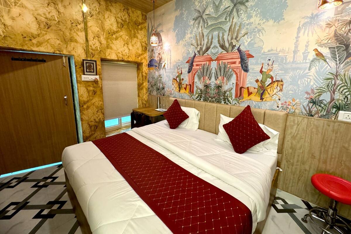Habitació d'hotel amb un llit gran, un mural a la paret, una porta de fusta i un tamboret vermell.