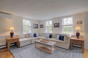 A living room with a sectional sofa, a coffee table, two side tables, and a large window with blinds. - Short drive to town and popular beaches! (Orleans)