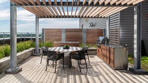 An outdoor patio with a round table and chairs, a grill, and a wooden fence. - 2BR Oasis w/ Gym & Terrace, Near Hintonburg! (Ottawa)