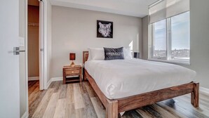 A modern bedroom with a large bed, wooden nightstands, a wall-mounted tiger artwork, and a city view through the window. - 2BR Oasis w/ Gym & Terrace, Near Hintonburg! (Ottawa)