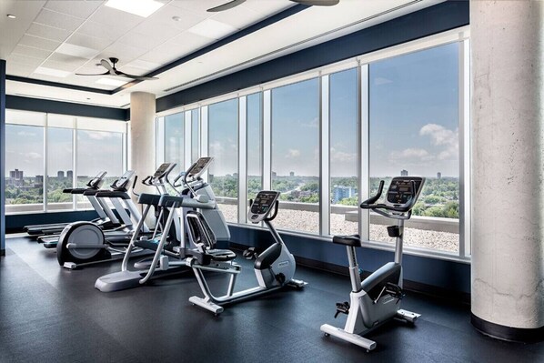 A gym with cardio machines and large windows offering a city view.