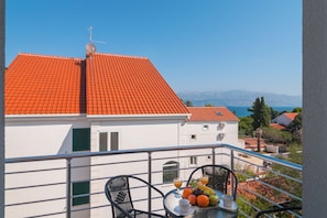 A balcony with a table set for breakfast, a clear view of the sea, and a red-tiled roof. - Apartments Island Beat (Supetar)