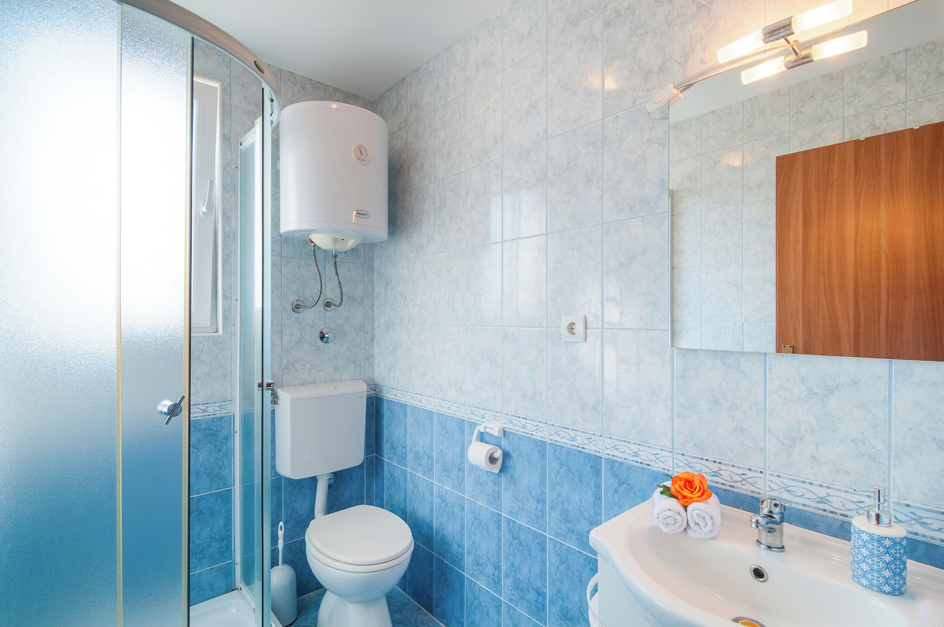 Een badkamer met een douchecabine van glas, een toilet, een wastafel met spiegel en een muur betegeld met blauwe tegels.