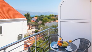 Un balcón con una mesa dispuesta para el desayuno, con vistas a un pueblo costero de edificios de tejados rojos y una vista despejada del mar.