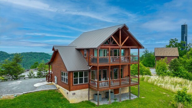 A two-story log cabin with a balcony, surrounded by lush greenery and a clear sky. - Private Getaway w/ Theater & Views Near Dollywood! (Sevierville)