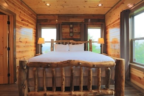 A rustic wooden bedroom with a large bed, two bedside lamps, and a window with curtains.
