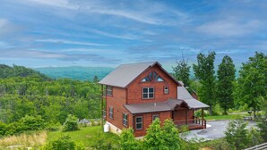 A two-story log cabin with a porch, surrounded by lush greenery and mountains in the background. - Private Getaway w/ Theater & Views Near Dollywood! (Sevierville)