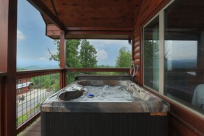 Ein Whirlpool auf einer Holzterrasse mit Blick auf Berge und ein Gebäude im Hintergrund.