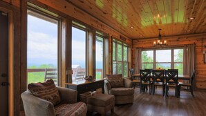 A cozy cabin interior with large windows, wooden furniture, and a dining table. - Private Getaway w/ Theater & Views Near Dollywood! (Sevierville)
