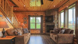 A log cabin interior with two sofas, a fireplace, a TV, and large windows. - Private Getaway w/ Theater & Views Near Dollywood! (Sevierville)