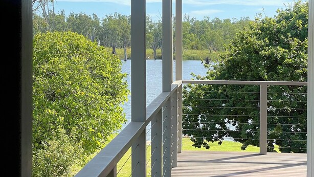 A covered wooden deck with a railing overlooking a lake and dense greenery. - Golden Mile - On the Waterfront (Bundalong)