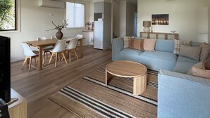 A spacious living area with a large sofa, a dining table with chairs, a ceiling fan, and a television. - Golden Mile - On the Waterfront (Bundalong)