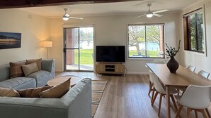 A spacious living room with a large sofa, a TV, and a dining area with a wooden table and chairs. - Golden Mile - On the Waterfront (Bundalong)