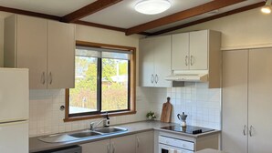 A modern kitchen with white cabinets, a built-in dishwasher, a window with a view, and a fruit bowl on the counter. - Golden Mile - On the Waterfront (Bundalong)