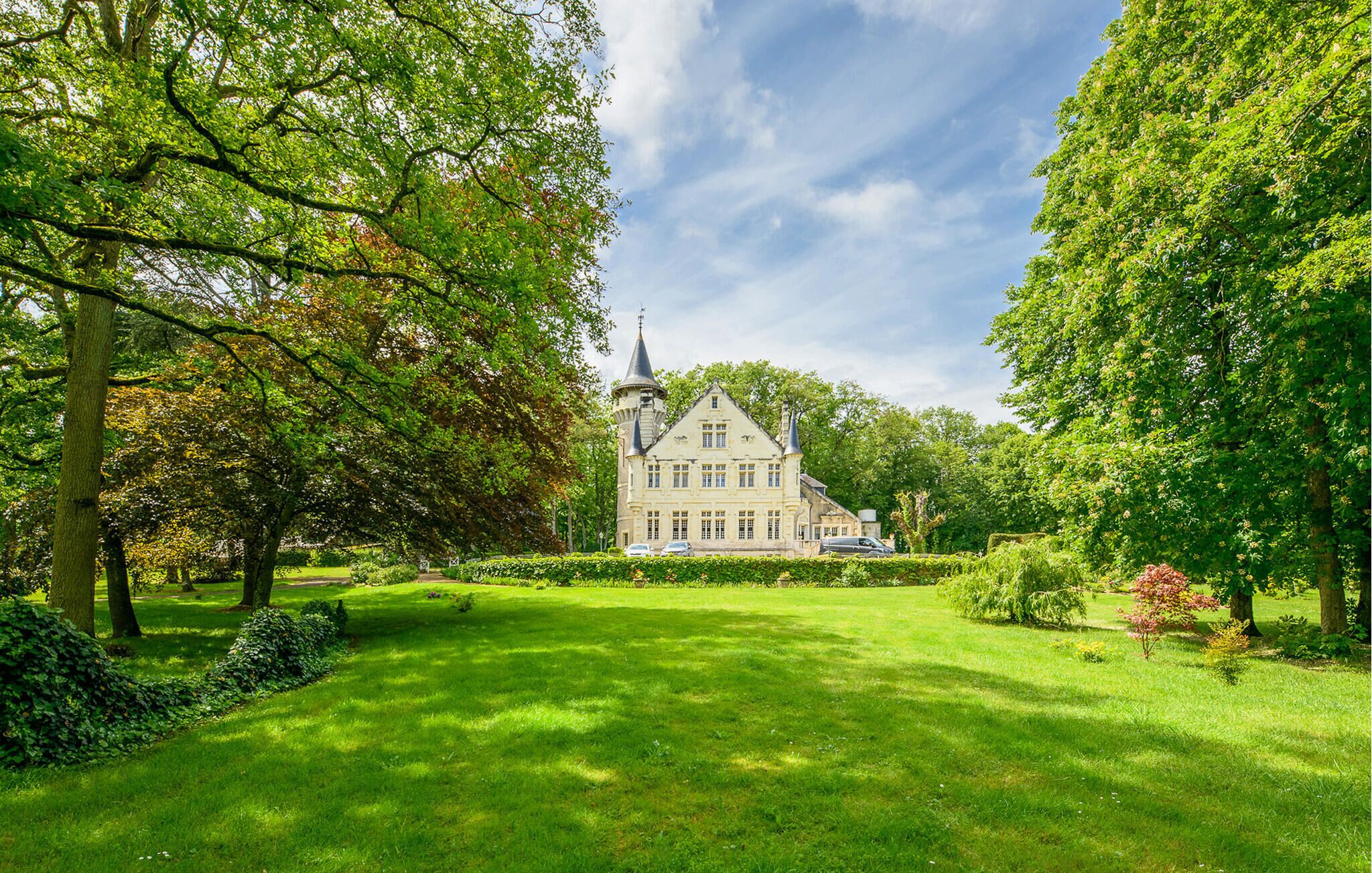 Ein großes, historisches Gebäude mit einem markanten Turm, umgeben von üppigem Grün und einem gepflegten Rasen.