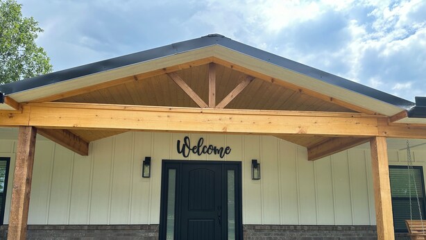 Une entrée d’immeuble avec une pancarte « Bienvenue » au-dessus d’une porte noire, des poutres en bois et une partie inférieure en briques.