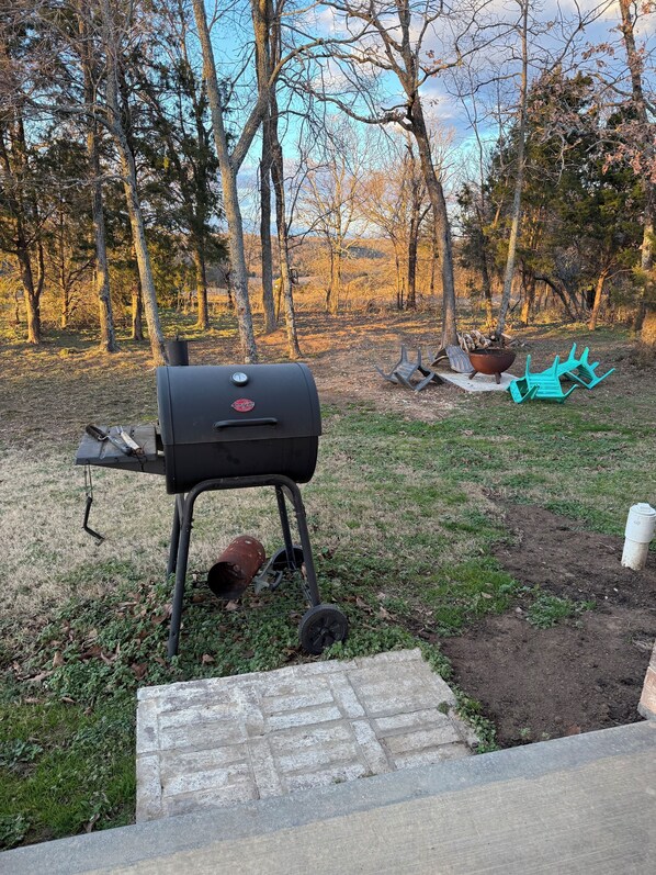 A barbecue grill in a backyard with trees and a fire pit.