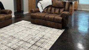 Un salon spacieux doté d’un parquet foncé, d’un canapé en cuir marron et d’un tapis à motifs.