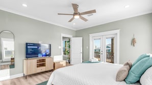 Une chambre à coucher comprenant un lit, un téléviseur, un ventilateur de plafond et une porte donnant sur un balcon.