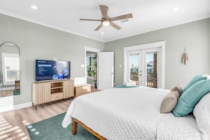 Un dormitorio con cama, televisor, ventilador de techo y puerta que da a un balcón.