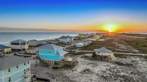 Une zone résidentielle côtière avec des maisons sur pilotis, une plage et un coucher de soleil.