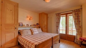 Ein Schlafzimmer mit einem hölzernen Bett, einem Nachttisch, einem Regal mit gerahmten Fotos und einem Fenster mit Vorhängen.