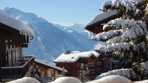 Eine Holzchalet mit Balkon, schneebedeckten Bäumen und Bergelandschaft im Hintergrund.