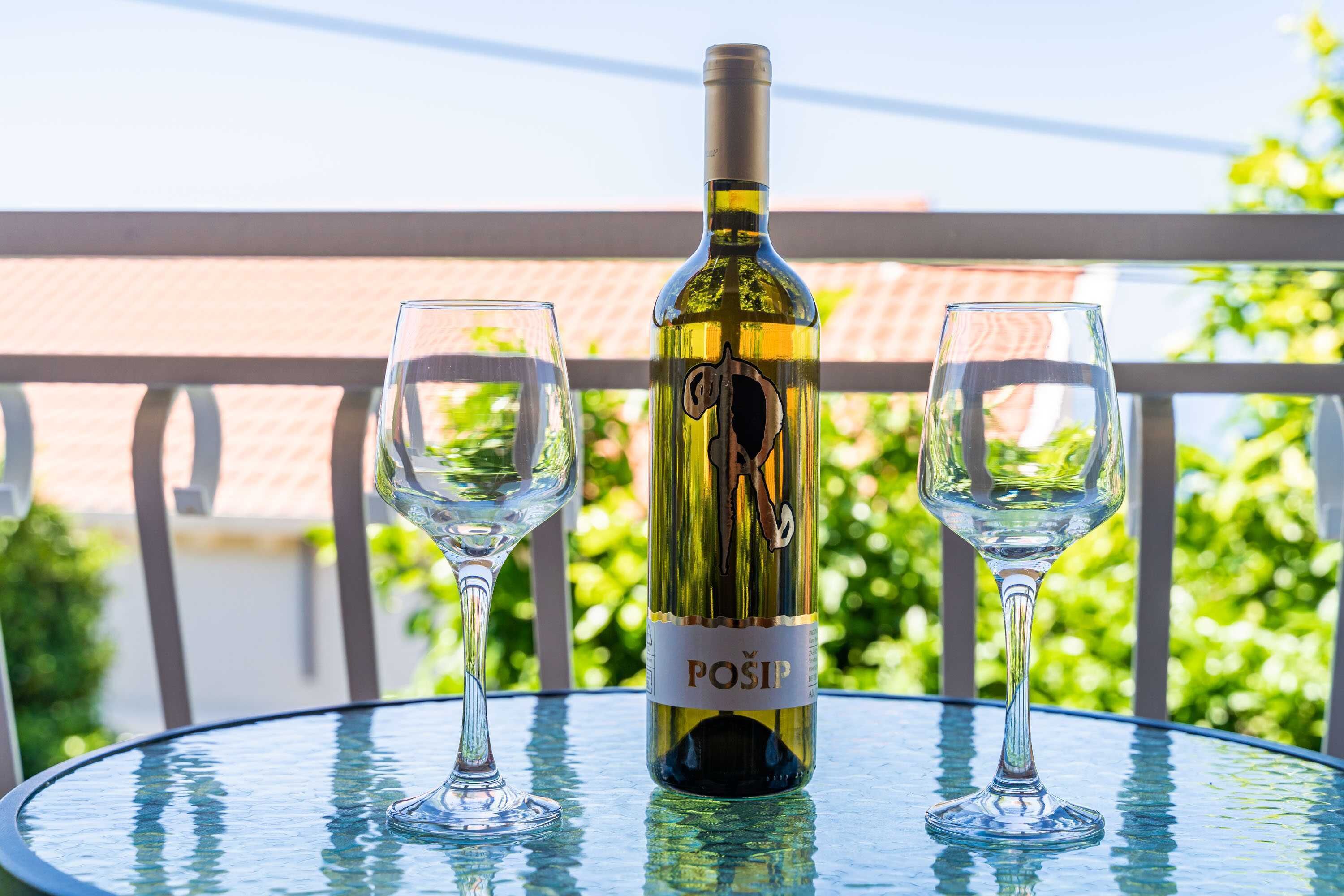 A bottle of wine and two glasses on a glass table with a balcony view.