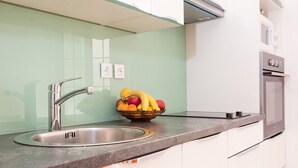 A modern kitchen with a stainless steel sink, a fruit bowl on the counter, and white cabinets. - Apartments Stella (Dubrovnik)