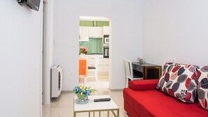 A compact living space with a red sofa, a small table with a vase of flowers, a remote control, and a TV mounted on the wall. - Apartments Stella (Dubrovnik)