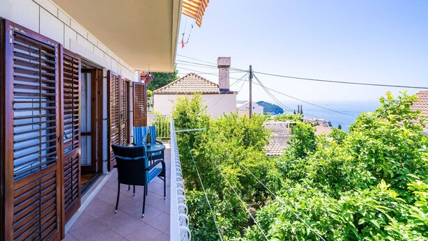 A balcony with a table and chairs, overlooking a garden and a coastal view. - Apartments Stella (Dubrovnik)