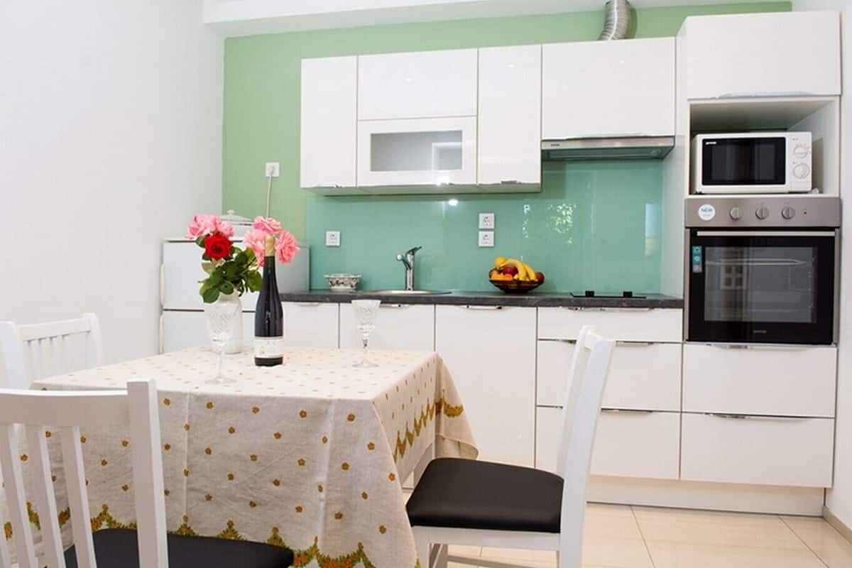 A compact kitchen with white cabinets, a microwave, an oven, and a dining table with chairs.