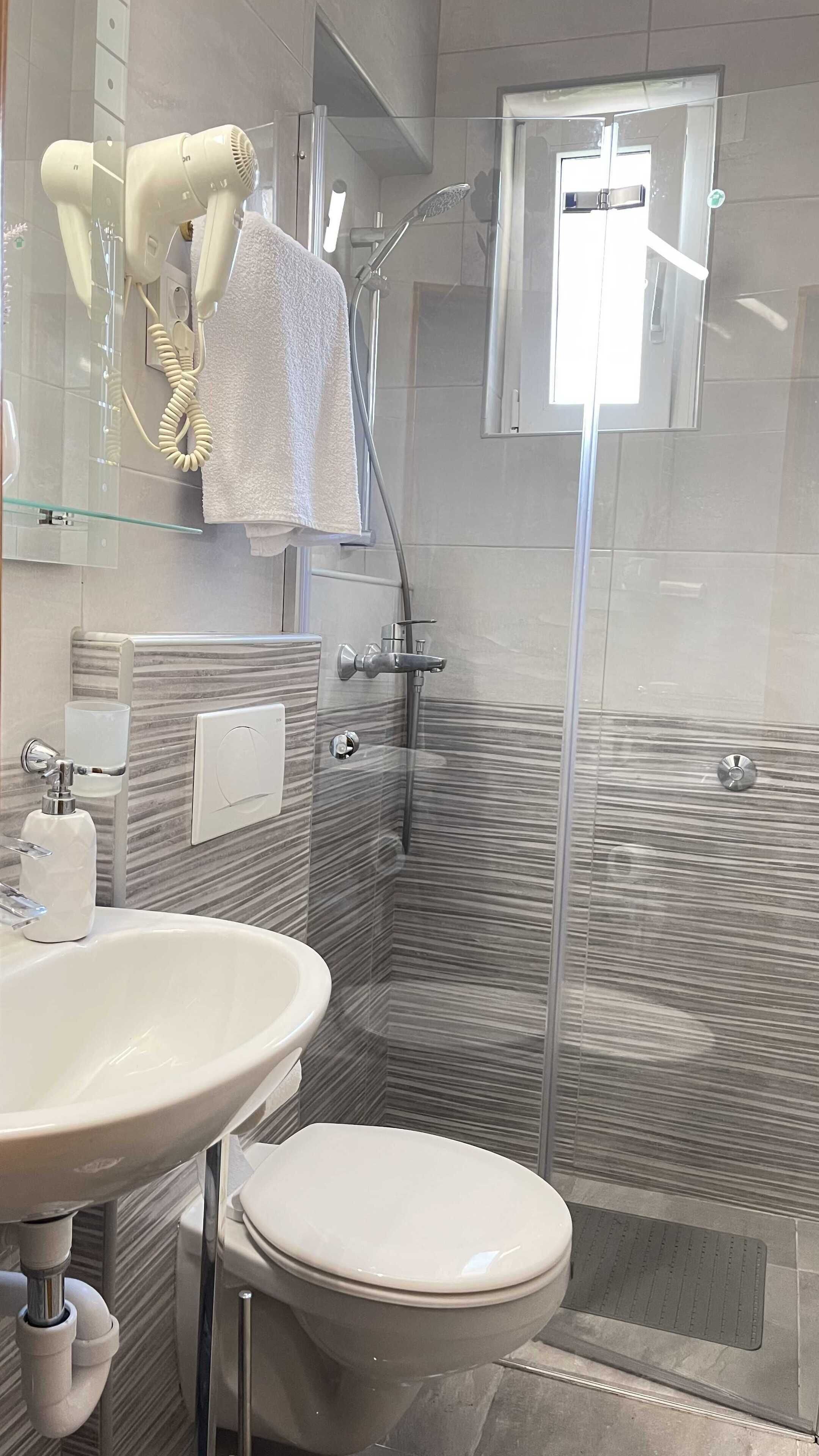 Un baño moderno con cabina de ducha de vidrio, un lavamanos blanco y un inodoro.